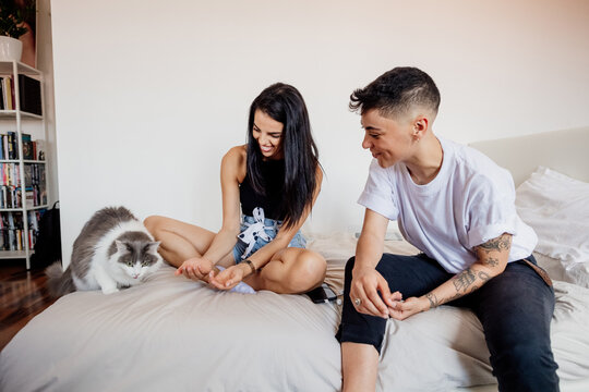 Young lesbian couple sitting on a bed, playing with cat.