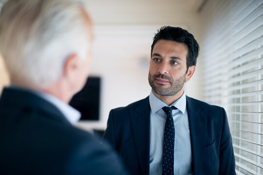 Two businessmen standing indoors, talking.