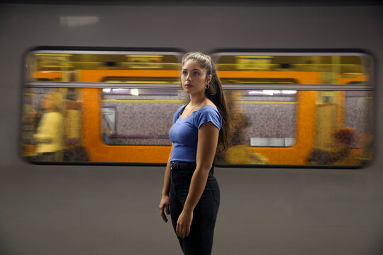 Young woman with long brown hair standing in front of commuter train on railway station platform.