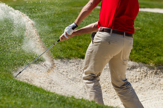 Male golfer chipping out of sand trap. 