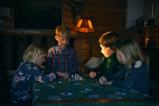 Group of children sitting at a table in a log cabin, playing chess, Vasterbottens Lan, Sweden. 