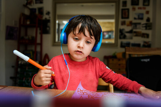 A five year old boy in blue headphones having an interactive learning session, home schooling. 