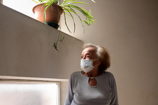 Senior woman wearing face mask standing in her home during Corona virus crisis. 