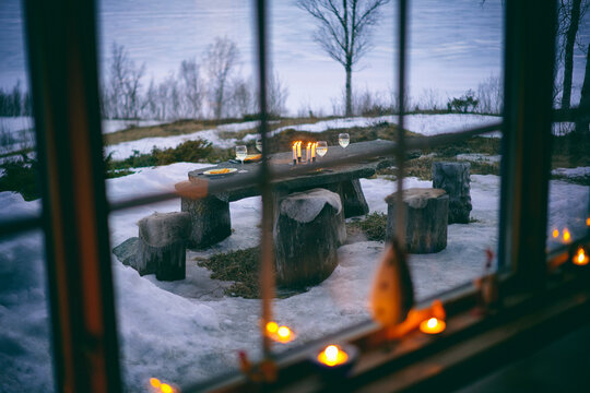 View through log cabin window onto outdoor table set with wine glasses and candles in Vasterbottens Lan, Sweden.