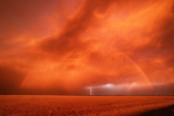A dust storm with vivid orange sky and rainbow, and cloud-to-ground lightning strike. 