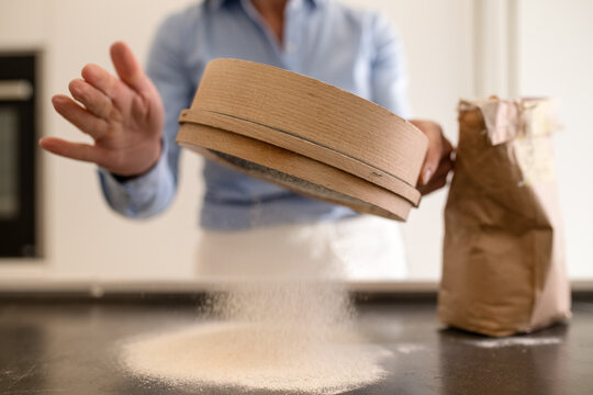 Woman standing in a kitchen, making fresh homemade pasta, sifting flour.