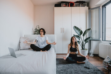 Two women with brown hair sitting in an apartment, meditating.