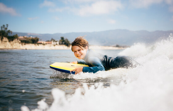 Portrait of young boy wearing wet suit, lying on surfboard, riding wave, Santa Barbara, California, USA.
