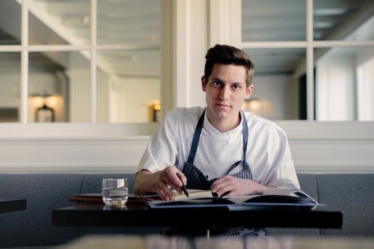 Young male chef doing paperwork and talking on smartphone in restaurant