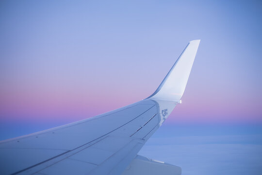 View along passenger plane wing flying above clouds at sunset.