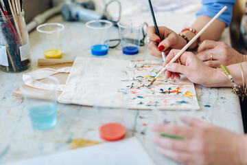 Two women painting on fabric bag in creative studio, mid section, close-up