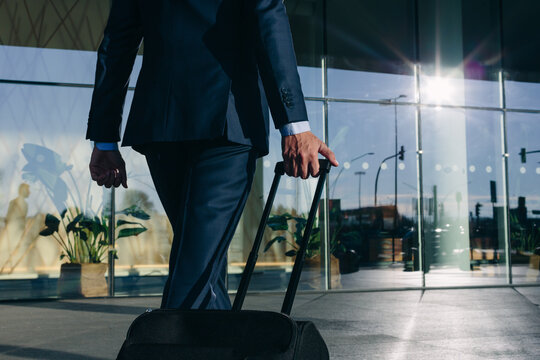Businessman with wheeled luggage walking towards glass building, Malpensa, Milan