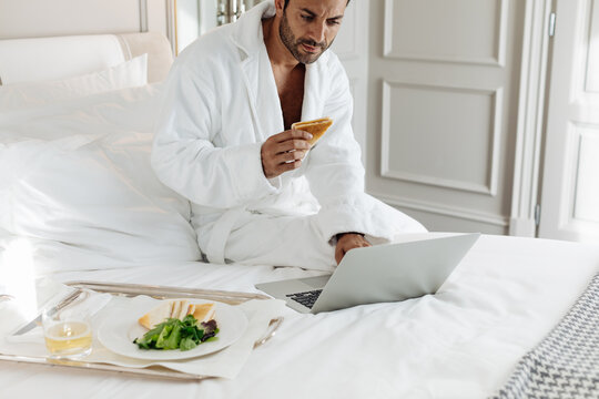 Man using laptop and having toast in suite