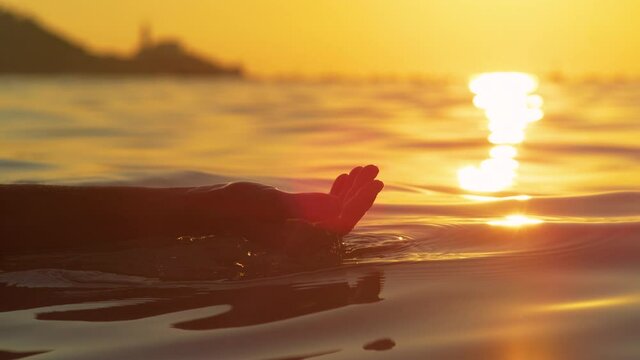 SLOW MOTION, CLOSE UP, LENS FLARE, DOF: Sunset shines on woman's hand cupping a handful of sea water. Unrecognizable female tourist on summer vacation lifts up a handful of ocean water at sunrise.