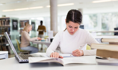 Obraz premium Adult female student with laptop and books in public library. High quality photo