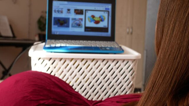 A young pregnant woman chooses a colorful rattle for her unborn child in an online store using a laptop and lying on the bed