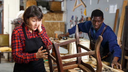 Outraged woman restorer standing near vintage armchair at workshop