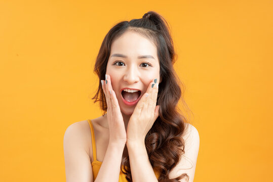  young pretty surprised woman with opened mouth standing with open palms, isolated on yellow background