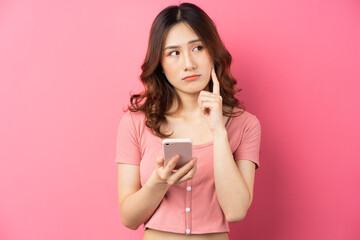 Young asian girl using the phone on pink background