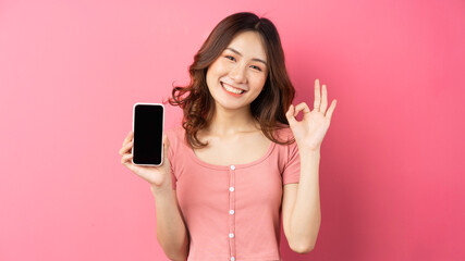 Young asian girl using the phone on pink background