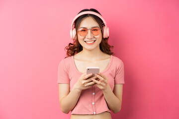 Young asian girl wearing headphones and using the phone on pink background - Powered by Adobe