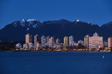 Fototapeta na wymiar Highrise buildings by ocean and mountains at dusk. West side Vancouver and grouse mountain from Kitcilano Beach. British Columbia. Canada 