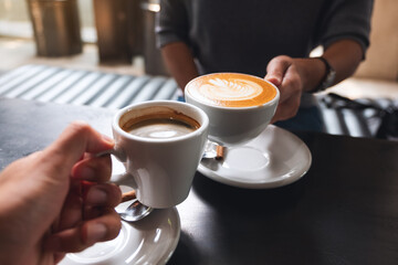 Closeup image of a man and a woman clinking white coffee mugs in cafe