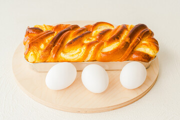 Baked yeast cake staffed with cream cheese - traditional French Brioche, and white eggs close up on wooden serving board on white background with copy space