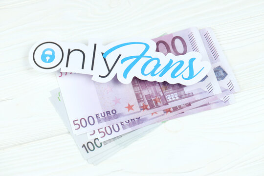 KHARKOV, UKRAINE - FEBRUARY 14, 2021: Onlyfans paper logo with euro bills on white wooden table. OnlyFans is content subscription service based in London