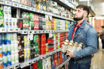 Stylish guy in denim jacket choosing beers during shopping in food store.