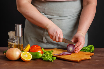 The chef cuts fresh vegetables on a wooden board. Cooking a burger.