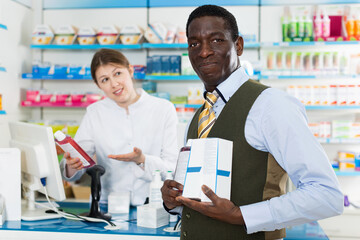 Portrait of positive smiling African American male customer buying medications in modern pharmacy