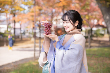 秋の公園でブドウを持つ女性
