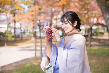秋の公園でブドウを持つ女性
