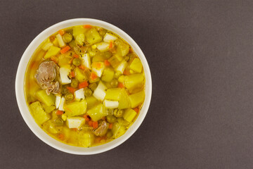 Chicken soup with vegetables in a white ceramic bowl on a gray b