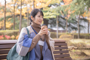 秋の公園でコーヒーを飲む会社員の女性（笑顔）
