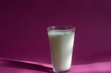 A glass of kefir on a pink surface with shadows.