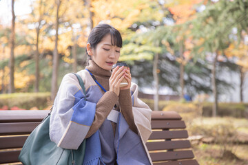 秋の公園でコーヒーを飲む会社員の女性（寒い）
