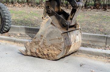 Dirty bucket excavator lowered onto the asphalt.