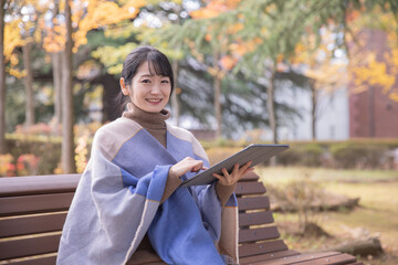 秋の公園でタブレットPCを使う女性（笑顔）
