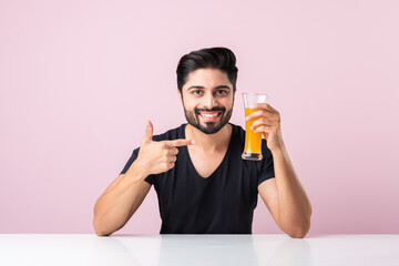 Handsome Indian asian man drinking healthy orange or mango juice from Glass
