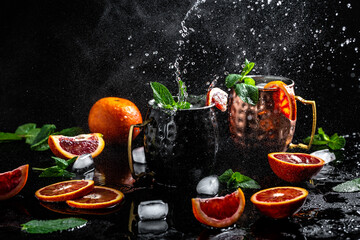 blood orange Moscow mule alcohol cocktails with fresh mint leaves and ice in copper mugs, splashes...