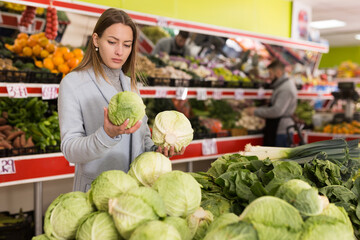 Portrait of adult woman buying fresh cabbage in grocery shop. High quality photo