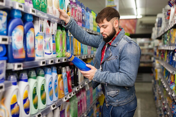 Stylish glad cheerful positive smiling bearded guy buying household chemicals in supermarket
