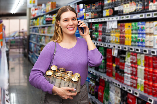 Happy woman buys canned beer in hypermarket and talking on mobile phone
