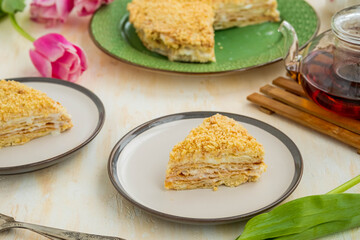 Sliced traditional chopped dough Napoleon cake with custard on a green plate on a light concrete background. Cake recipes.
