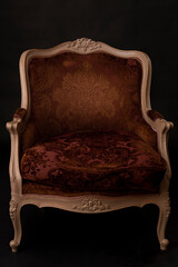 A vintage embossed red velvet chair in the French style against a black bacdrop