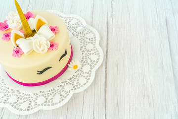 Unicorn cake on a wooden background and lace. Cute unicorn layered homemade cake decorated with bow, rose flowers, golden corn and ears. Copy space