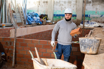 Focused young man working on his house renovations, installing brick wall inside ..