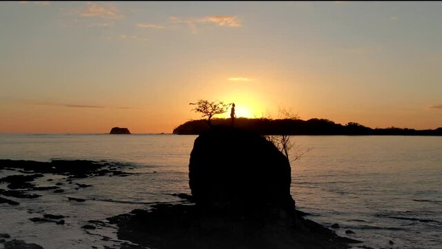 Beautiful and peaceful aerial view of a woman practicing yoga and meditation on a rock over the sunset in a beach  
